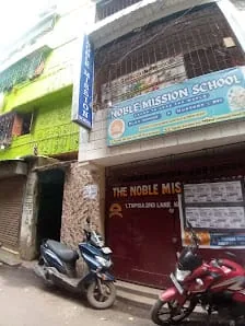 Street-level view of the Noble Mission School Campus 1 gate with blue signage reading Learn to Lead the World