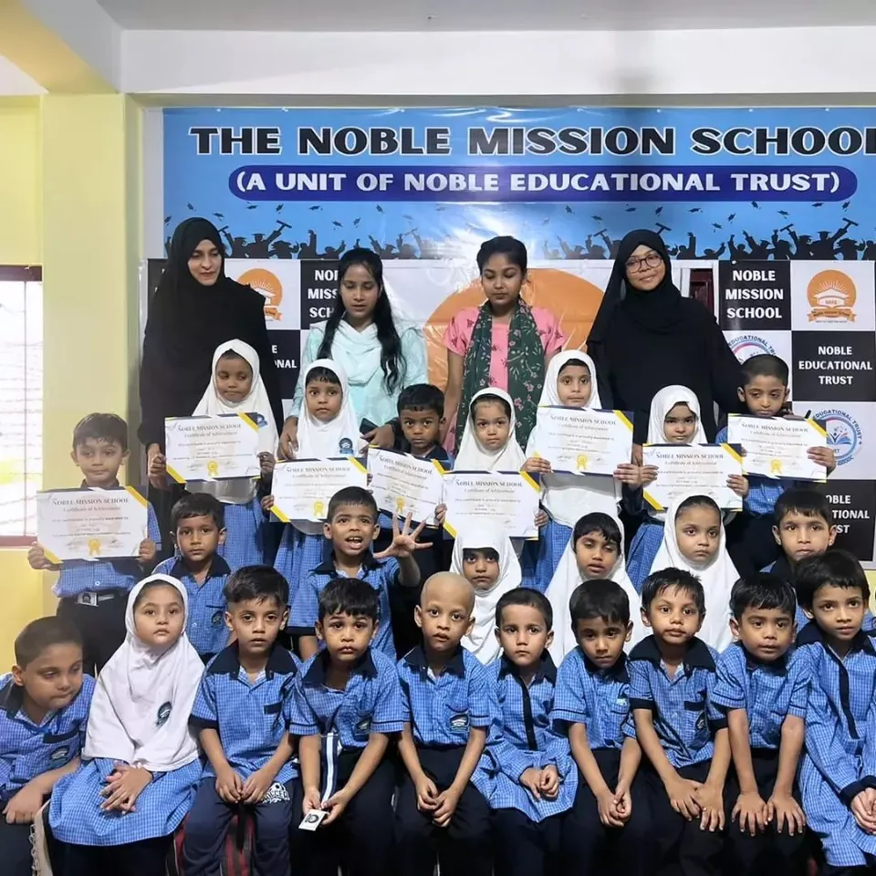 Group photo of junior NMS students in blue uniforms holding certificates, with teachers standing behind them under the school banner