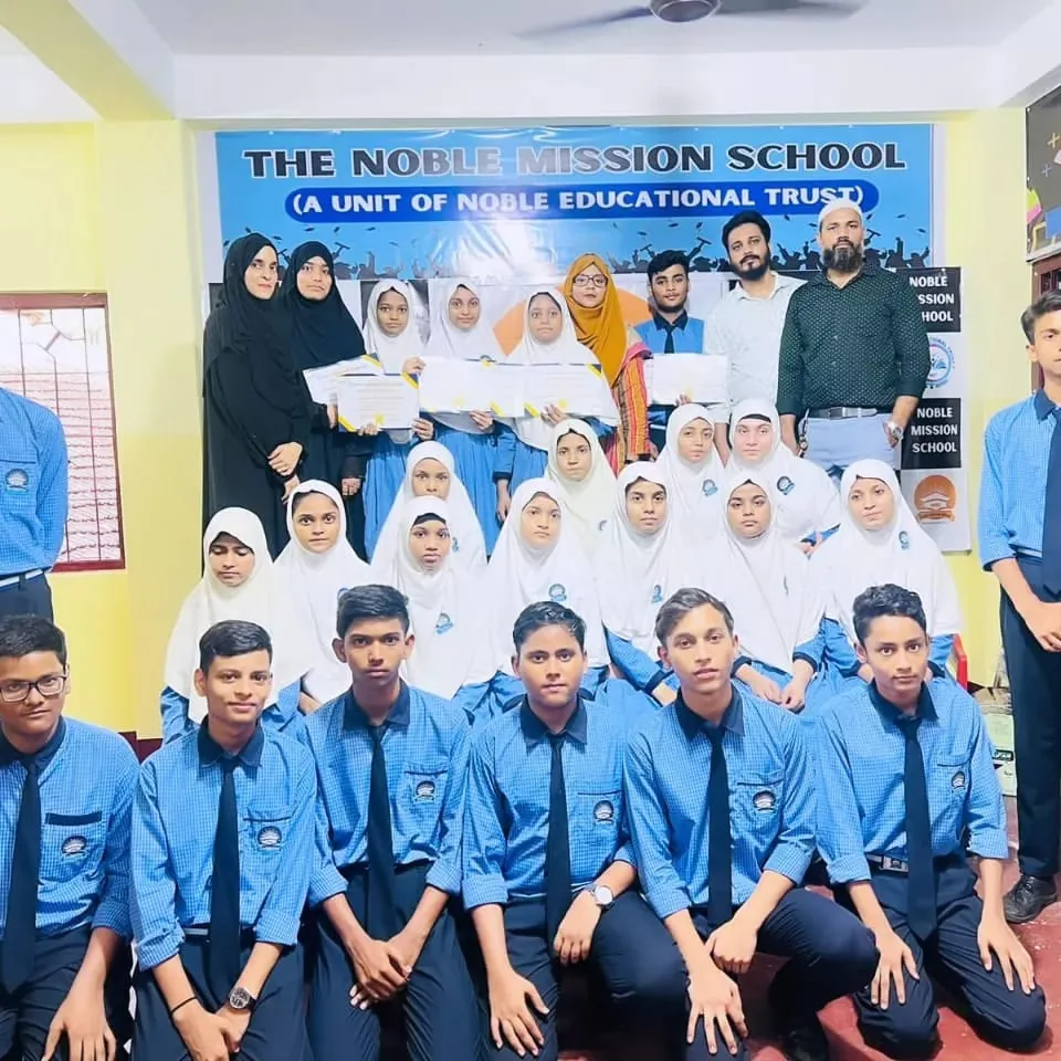 Senior NMS students in blue shirts and white hijabs posing with teachers for a class group photo beneath the school banner