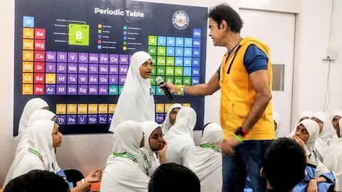 NMS student speaking into a microphone during a science session with a periodic table poster behind