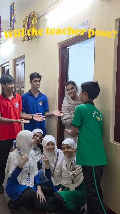 NMS students in colourful uniforms laughing with a smiling teacher in a school corridor