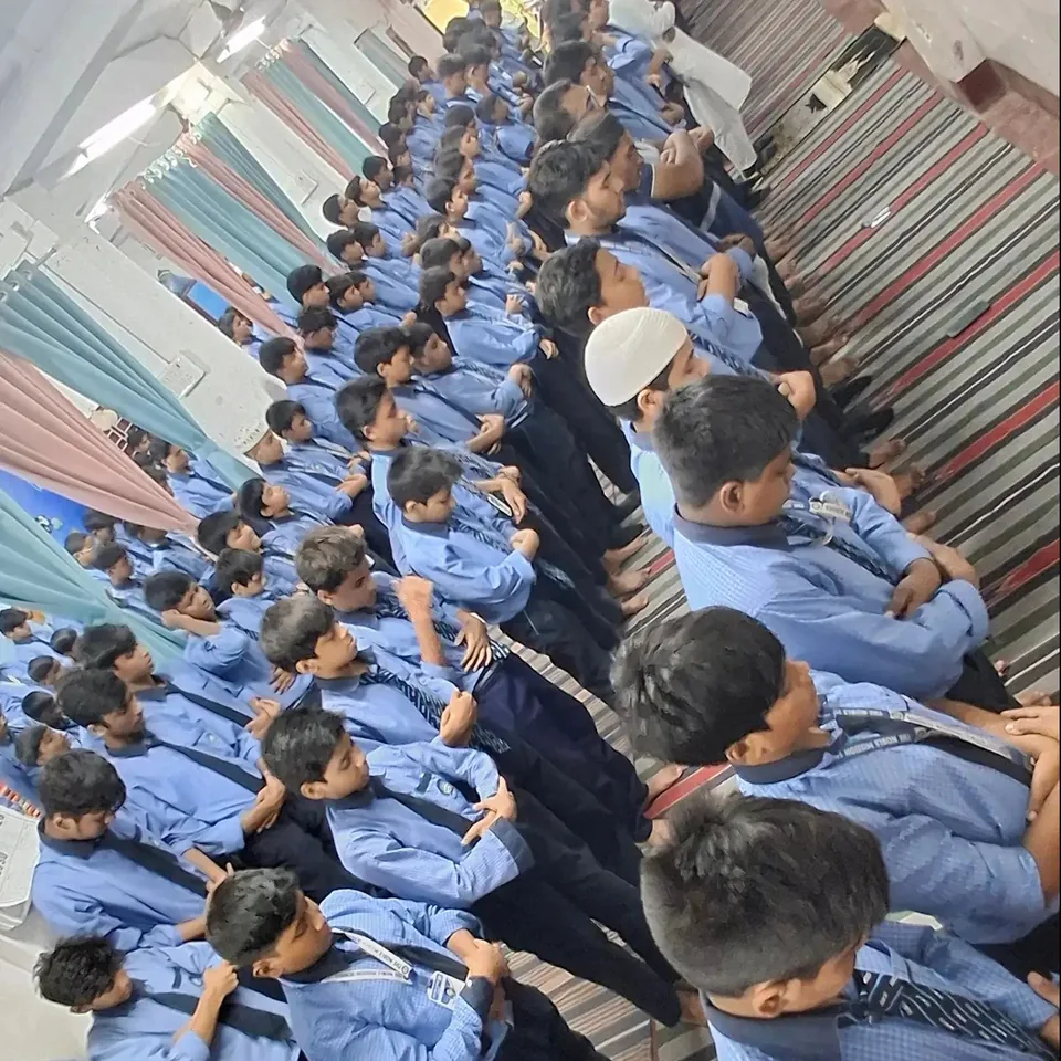 Students of The Noble Mission School standing in prayer rows on striped rugs for Zohar Salah